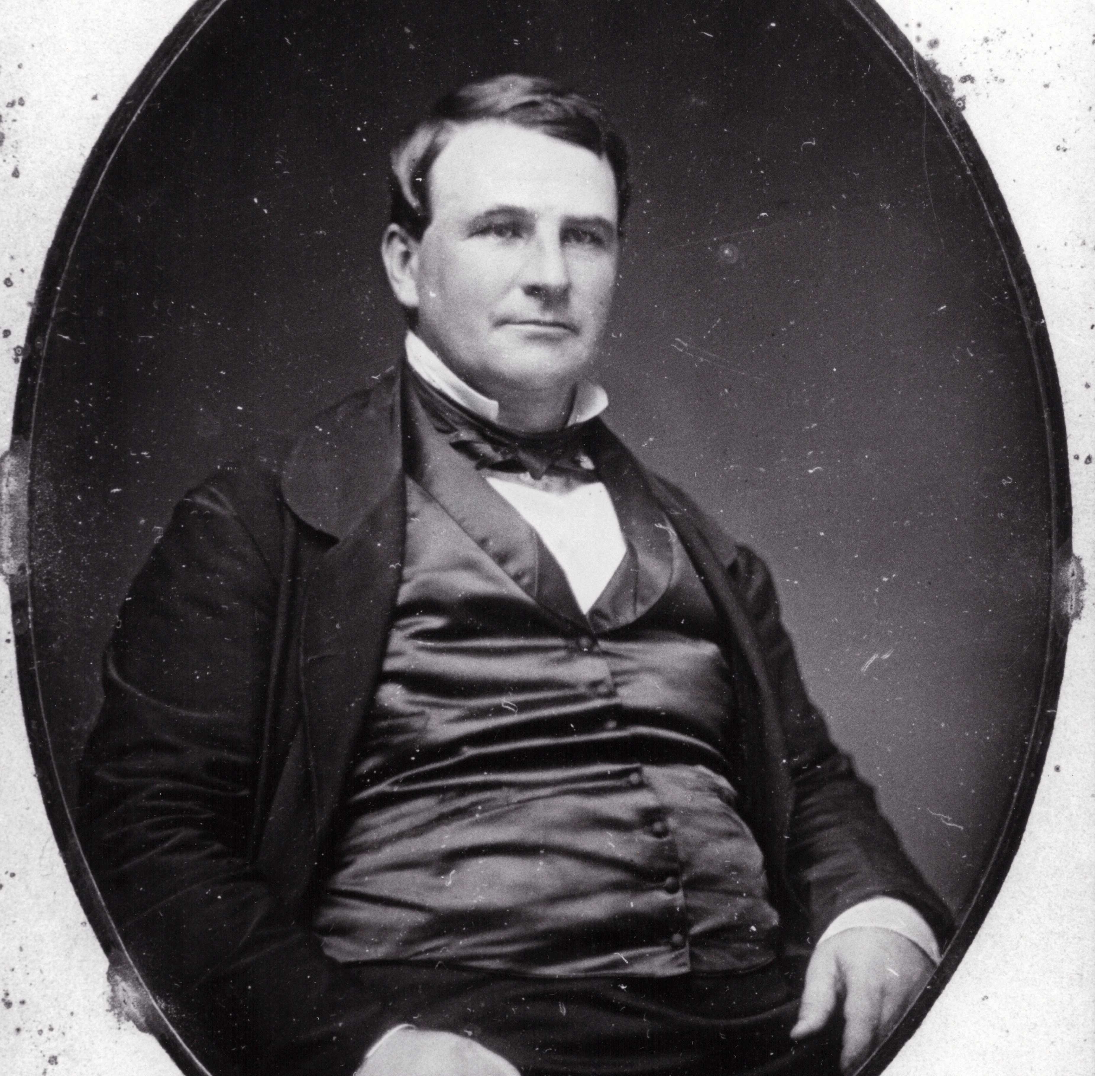 a portrait of a white man wearing a black suit. he has short dark hair.