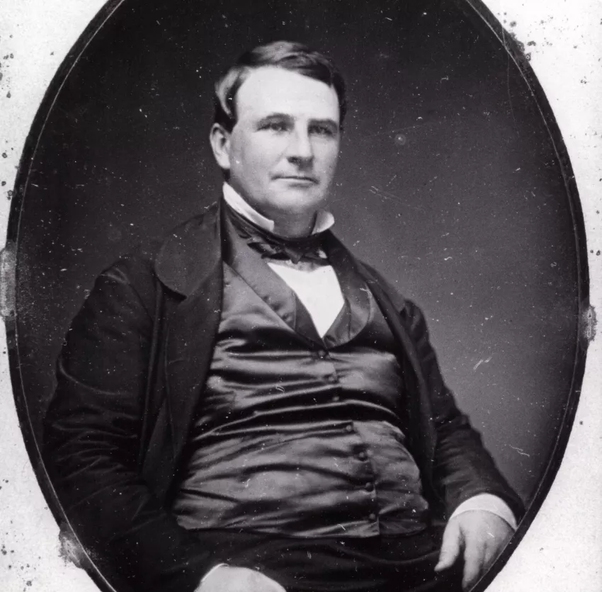 a portrait of a white man wearing a black suit. he has short dark hair.