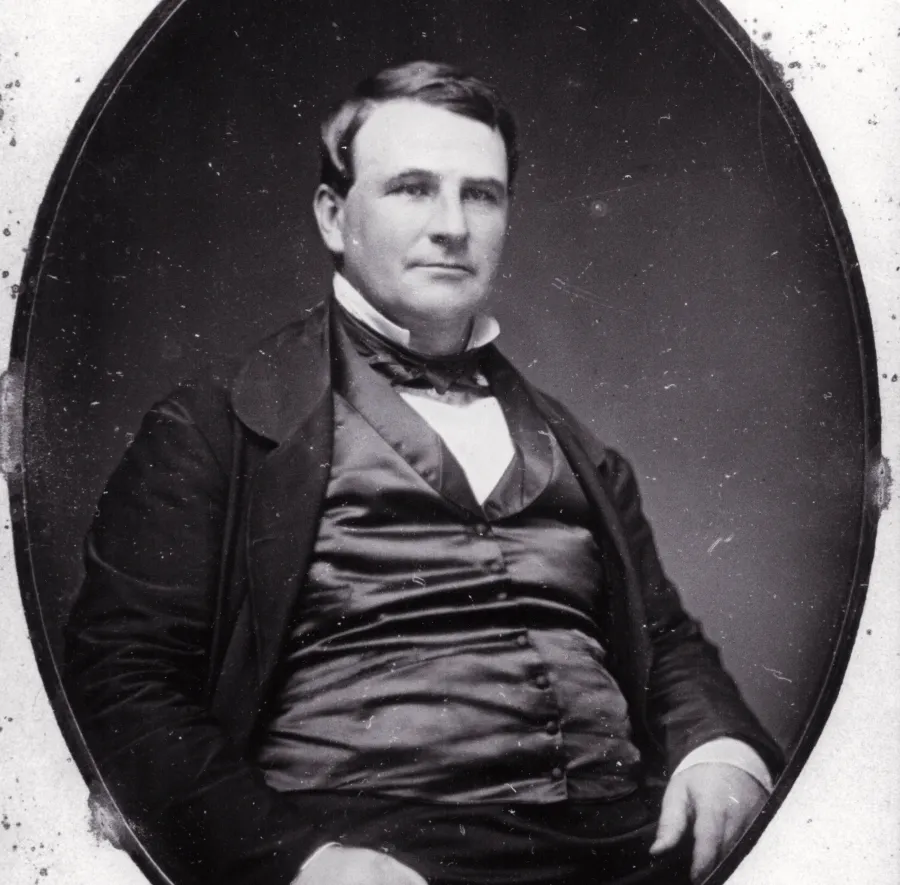 a portrait of a white man wearing a black suit. he has short dark hair.