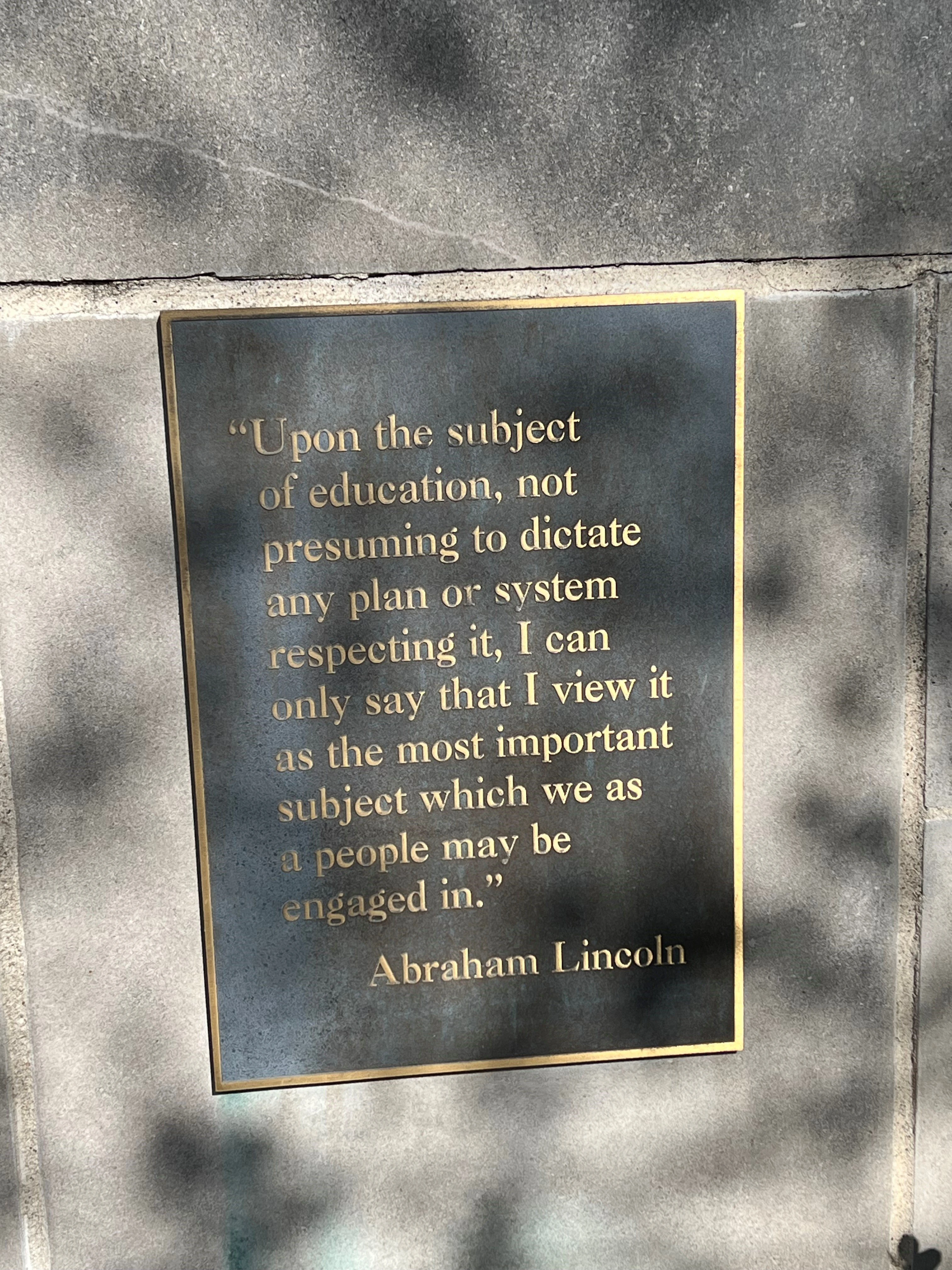 Bronze plaque mounted on concrete wall with gold-lettered quote from Abraham Lincoln about education being the most important subject for people to engage in.