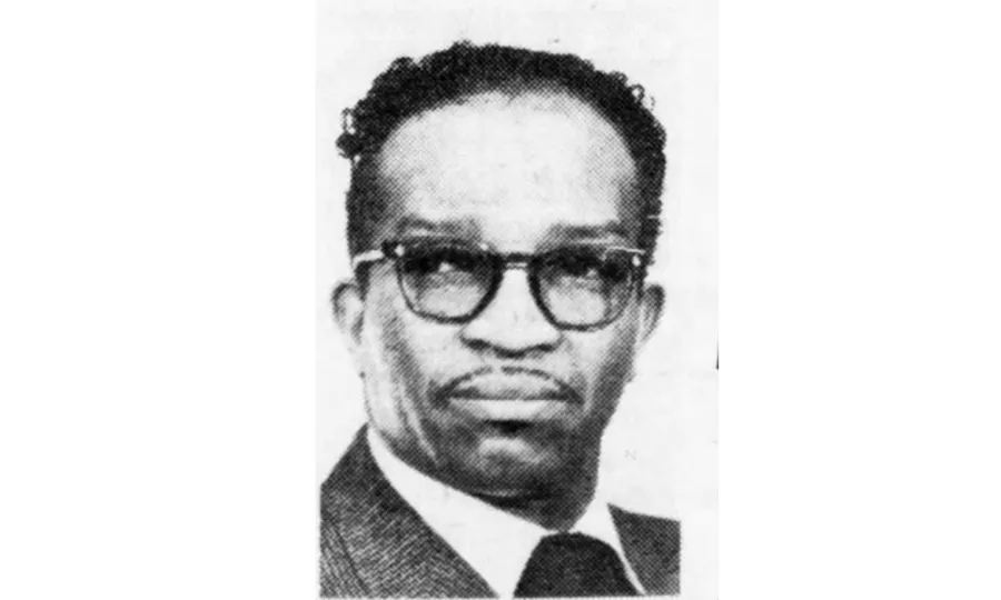 Black and white portrait of a Black man in a suit, wearing black glasses, a slender mustache, and curly hair.