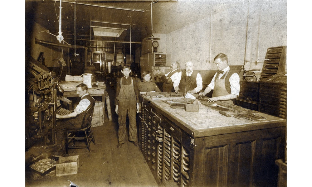 Four men and two boys working in a print shop.