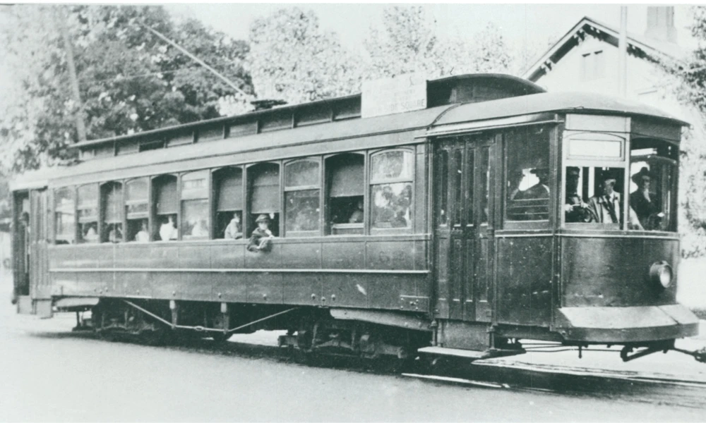 Black and white photo of a streetcar filled with people. Some window shades are open, some are closed.
