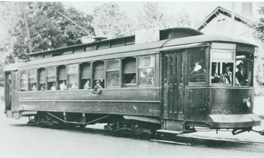 Black and white photo of a streetcar filled with people. Some window shades are open, some are closed.