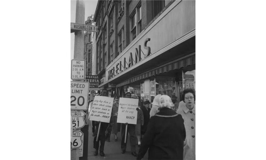 Black and white photograph of a civil rights protest on a city street. Protesters hold signs including one marked 