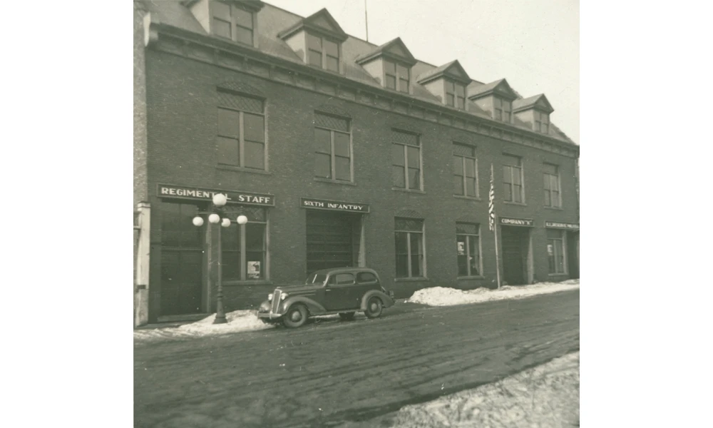 Brick building with dormer windows and snow on the ground, featuring storefronts labeled 
