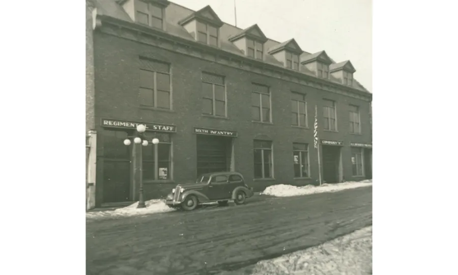 Brick building with dormer windows and snow on the ground, featuring storefronts labeled 