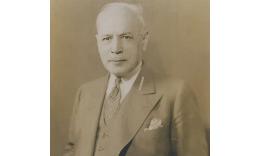 Sepia portrait of a mostly bald man in a three-piece suit with checkered tie.